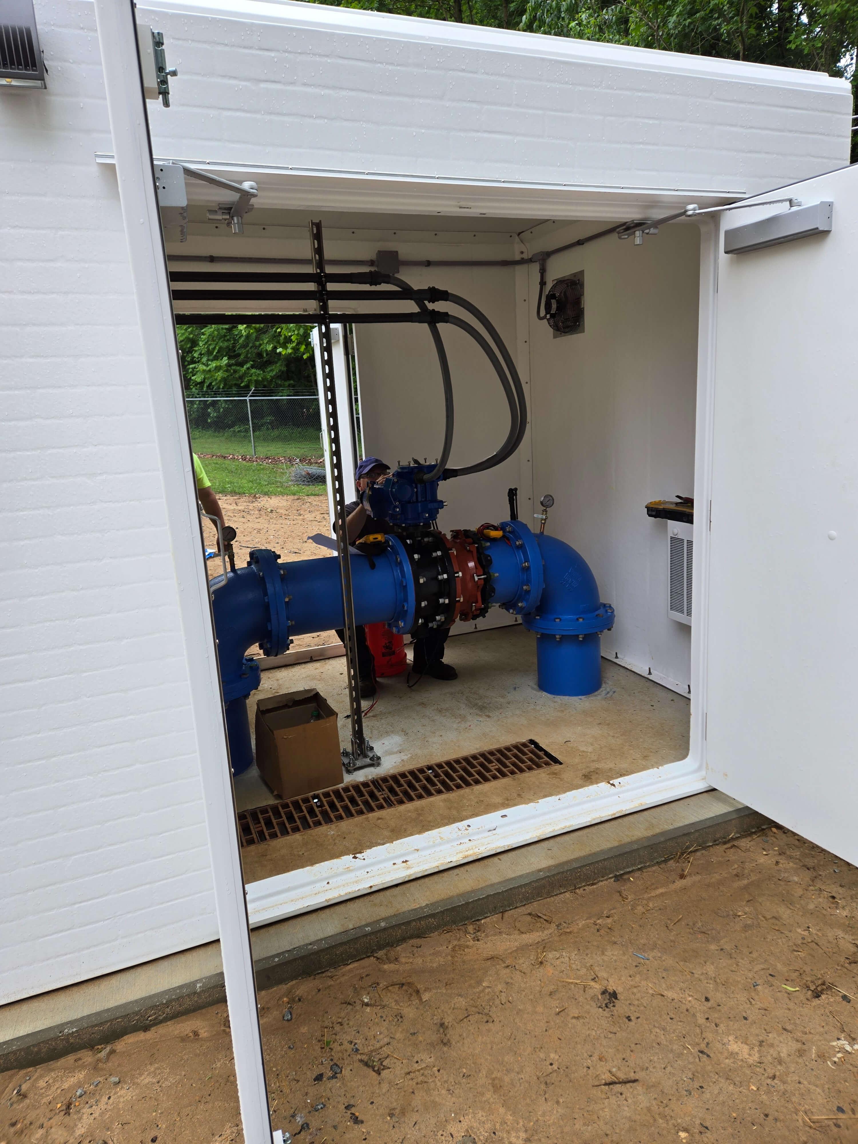 Interior view of fiberglass valve shelter showing motorized butterfly valve, control lines, wall heater, and open double doors