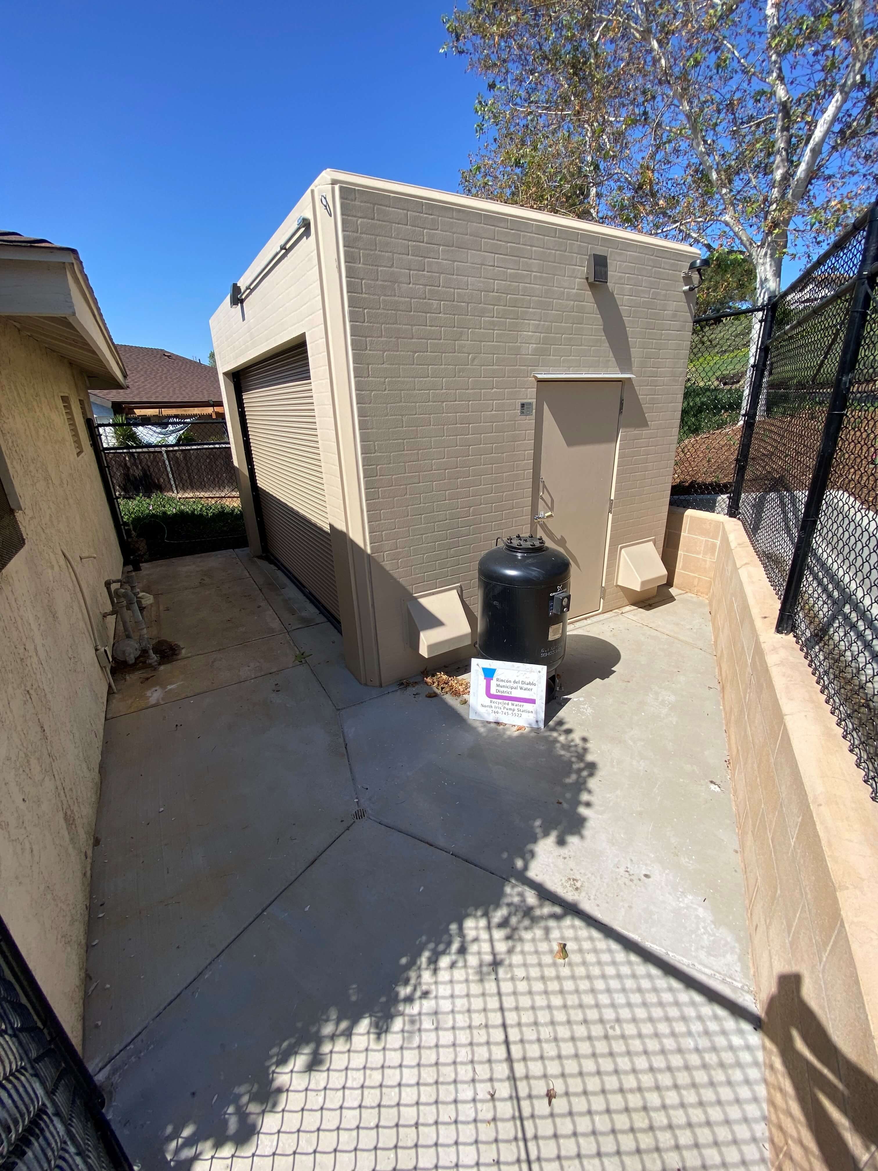 Beige fiberglass pump station enclosure with roll-up door on concrete pad