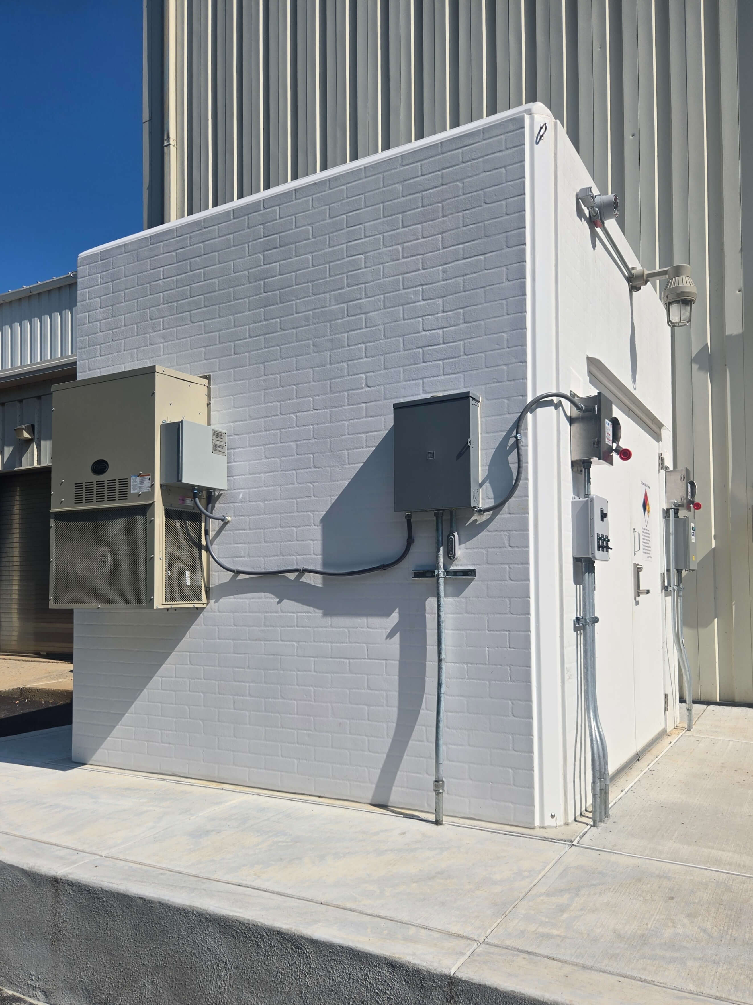Beige fiberglass pump station enclosure with roll-up door on concrete pad