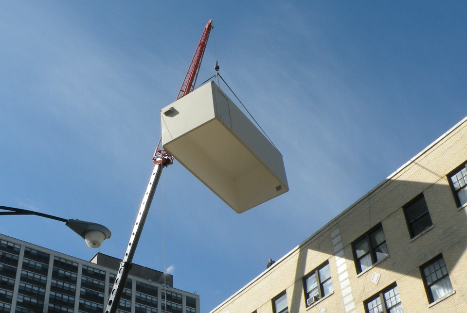 telecom shelter being lifted onto a rooftop by crane
