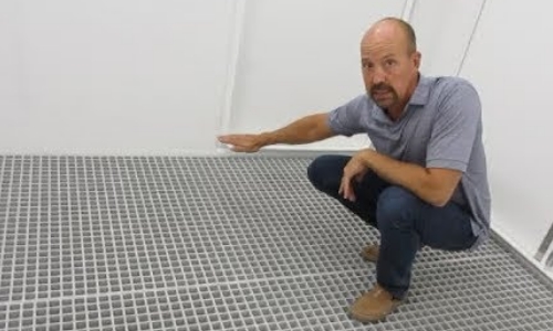 still frame from video - a man crouched insided a shelter to point out details of dimaond plate containment flooring