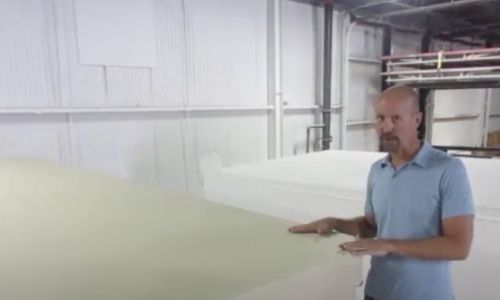 still frame from video - a man inside a warehouse shows a shelter roof while explaining customization options