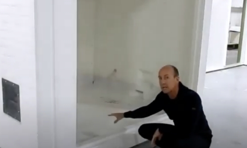 still frame from video - a man crouching in front of a shelter explaining options for door placement and style