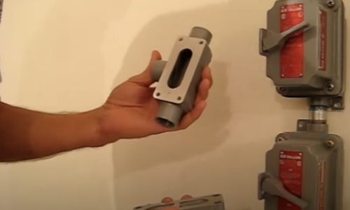 still frame from video - a person holds up electrical safety equipment while showing electrical systems within the shelter