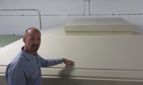 still frame from video - a man points to the rooftop hatch on the exterior of a shelter