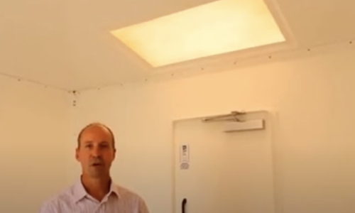 still frame from video - a man stands inside a shelter demonstrating the ambient light available through shelter skylights