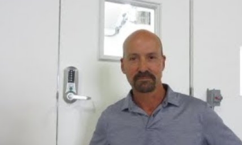 still frame from video of a man standing in front of a shelter door with a numeric push button lock on the handle