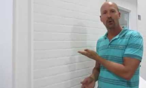 still frame from video - a man gestures to a bulkhead (dividing wall) in a shelter